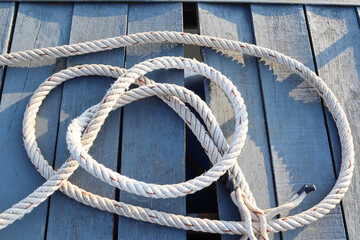 Ship ropes tied to knot on wooden flooring background closeup, at the port.