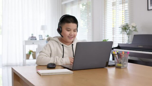 Young asia boy student wear headset headphone with computer laptop videocall talk present online e-learning class study with teacher, social distance learn language at home, homeschooling concept.