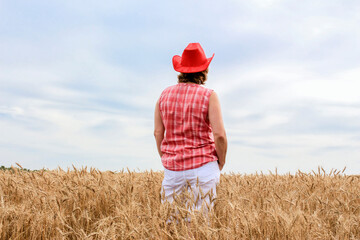 Caucasian woman wearing red cowboy hat standing in a wheat field..