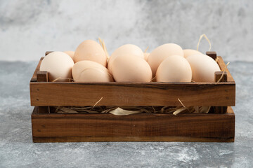 Wooden box of organic raw eggs on marble surface