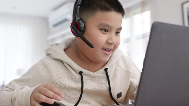 Young asia boy student wear headset headphone with computer laptop videocall talk present online e-learning class study with teacher, social distance learn language at home, homeschooling concept.