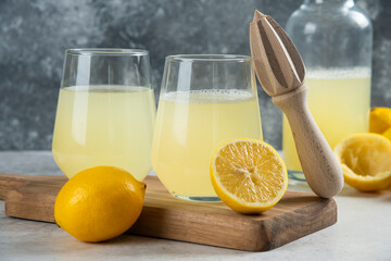 Two glass cups of lemon juice and wooden reamer
