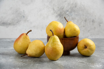 Bunch of fresh bio pears in wooden bowl on marble surface