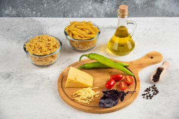 Raw pasta, oil, cheese and fresh vegetables on marble background