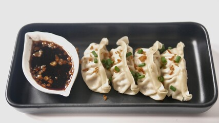 Steamed Gyoza or dumpling stuffed ground pork dipping with garlic soy sauce on white background.