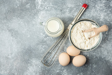 Flour, eggs, milk and whisker on marble background
