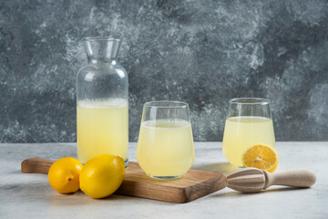 Two glass cups of lemon juice and jar on a wooden board