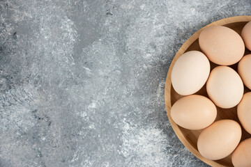 Wooden plate of fresh organic raw eggs on marble surface