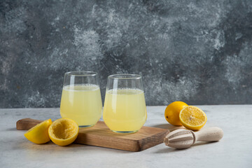 Two glass cups of fresh lemon juice on a wooden board