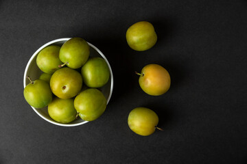 Green plums in a white ceramic saucer, top view