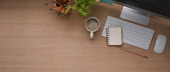 Horizontal photo of wooden office desk with computer, coffee up, notebook, plant and copy space.