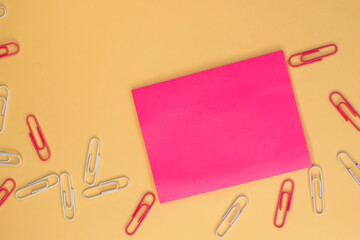 On a yellow background among the colored paper clips there is a sticky pink sheet for notes. Space...