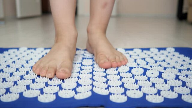 Unrecognizable teenage boy stands barefoot on a spiked rug slow motion.