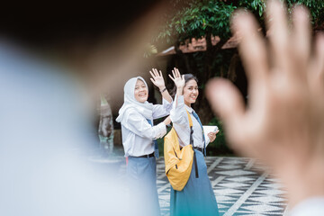view of shot from beside the waving hand a high school student with two female high school students wearing a school bag waving