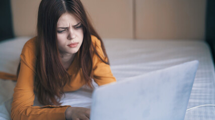 woman in the bedroom lies in bed in front of a laptop internet technology work