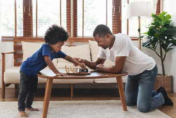African American Father and son playing chess in living room together. Happy Black Family engaged...