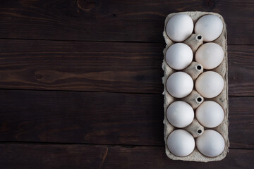 Fresh chicken eggs in a package, raw eggs in a white shell in a box. Top view copy space, wooden background.