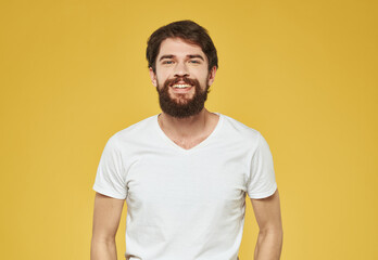 Obraz premium A man in a white T-shirt gestures with his hands on a yellow background Copy Space