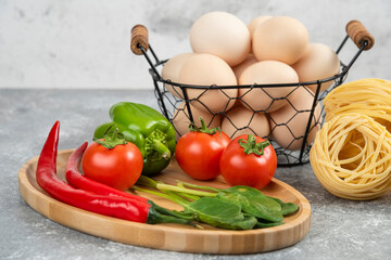 Plate of fresh vegetables and noodle nests on marble surface