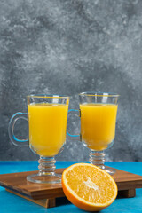 Two glass cups of orange juice on a wooden board