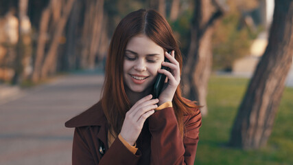 pretty woman in a coat With a phone in hand walking in the park rest