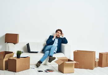 A man sits on the couch in front of a laptop working boxes with things unpacking a new office