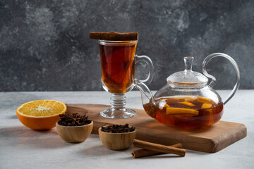 A teapot with tea and slice of orange on a wooden board