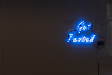 Get tested blue neon letters message sign on plain wall. Coronavirus, hiv, diseases prevention concept. Copy space for text