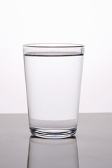 Blank glass of water captured with reflection with back lighting against light background.