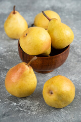 Bunch of fresh bio pears in wooden bowl on marble surface