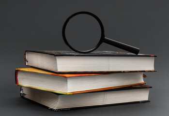 Magnifying glass on stack of books on black background. - 419993970