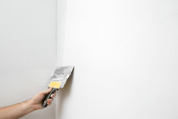Young adult man hand using spatula and plastering corner of wall with white fresh finishing putty....
