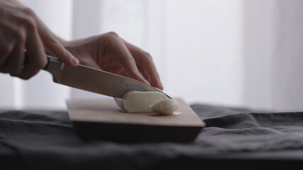 man slicing mozzarella ball on olive wood board with window on background