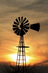 Kansas Windmill silhouette with a tree and colorful sky with clouds north of Hutchinson Kansas USA out in the country.