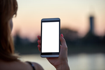 Young woman holding cellphone with blank white screen in urban city surroundings.