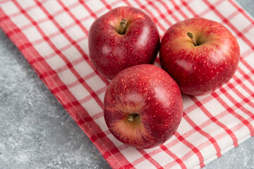 Three red apples with striped tablecloth on marble surface