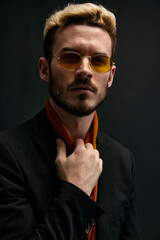 Obraz premium stylish man with glasses blond black jacket orange sweater dark background