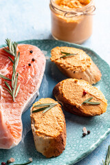 Homemade fish pate with herbs. Salmon pate on bread, Smoked salmon and soft cheese spread, mousse, pate in a jar with sliced bread on blue background. vertical image, place for text