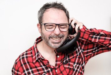 Obraz premium Portrait of a laughing mature man with bear wearing red plaid shirt and glasses. Wearing headphones.
