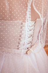 Close-up image of the detailed laces on the back of a wedding dress. Bride getting ready.
Bow on the back of the bride's wedding dress, the bride's morning gathering
