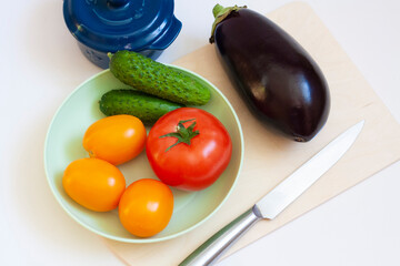 Cooking vegetables, tomatoes and cucumbers in a plate, eggplant, pot, cutting board and knife