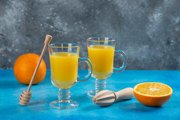 Two glass cups of orange juice with wooden reamer