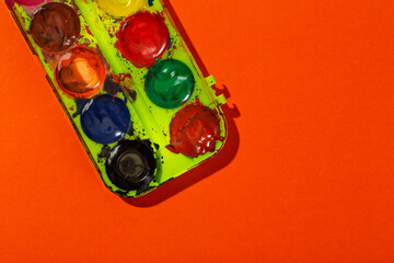 Watercolor in a box. Watercolor paints on an orange background. Space for text.