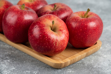 Wooden plate of shiny red apples on marble background