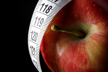 apple and tape measure on black background