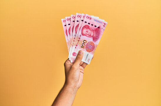 Hand of hispanic man holding chinese 100 yuan banknotes over isolated yellow background.