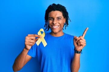 Young african american man holding suicide prevention yellow ribbon smiling happy pointing with...