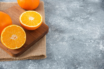 A wooden board full of juicy slices of orange fruit on stone background