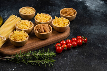 Pasta varieties in wooden cups served with cherry tomatoes and rosemary leaves