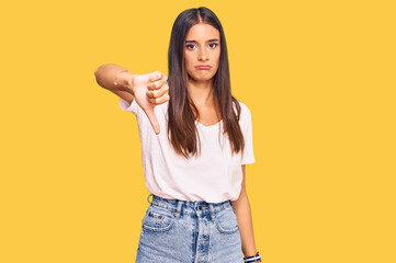 Young hispanic woman wearing casual white tshirt looking unhappy and angry showing rejection and negative with thumbs down gesture. bad expression.